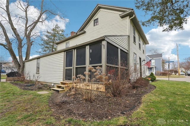 view of side of property featuring a sunroom, a chimney, and a yard