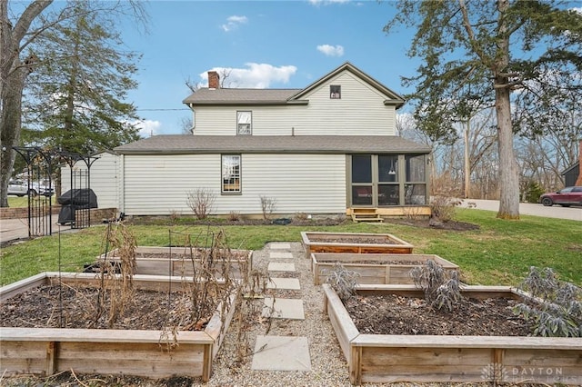 back of house featuring a sunroom, a chimney, a vegetable garden, and a yard