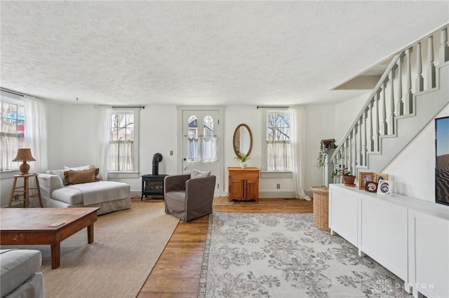 living area with baseboards, wood finished floors, a wood stove, stairs, and a textured ceiling