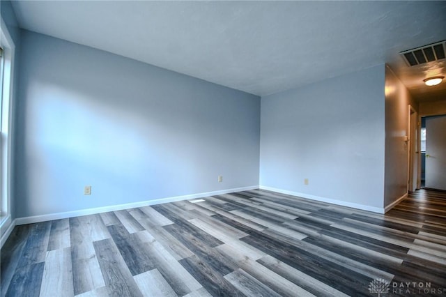 empty room with dark wood-style floors, visible vents, and baseboards