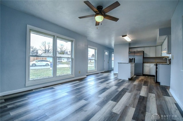 unfurnished living room featuring ceiling fan, dark wood finished floors, visible vents, and baseboards