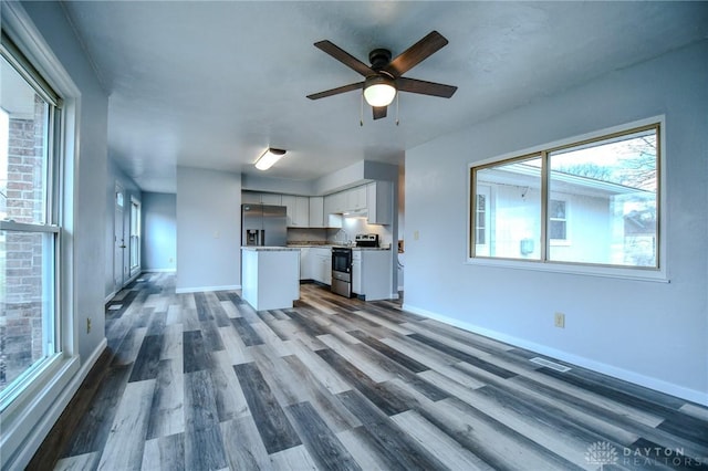 unfurnished living room with dark wood-style floors, a ceiling fan, and baseboards