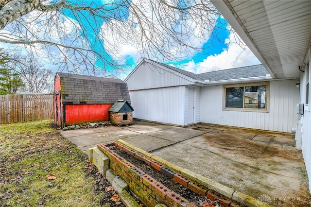 exterior space featuring an outbuilding, a patio, a storage shed, a shingled roof, and fence