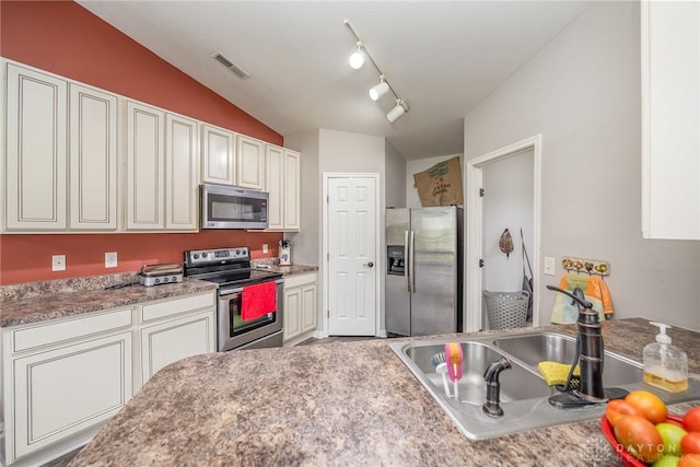 kitchen with stainless steel appliances, lofted ceiling, visible vents, a sink, and track lighting