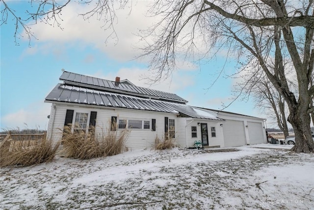 snow covered property with a garage, a chimney, and metal roof