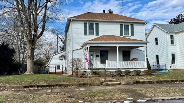 american foursquare style home with roof with shingles, covered porch, a front yard, and fence