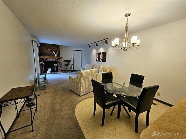 dining area featuring a notable chandelier, track lighting, a textured ceiling, light colored carpet, and a brick fireplace