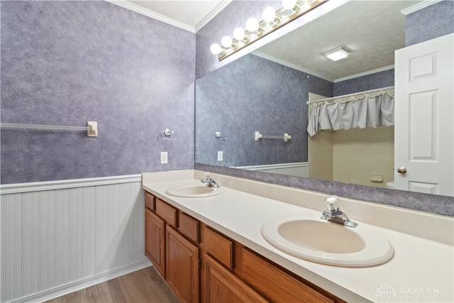 bathroom with a wainscoted wall, wallpapered walls, ornamental molding, and a sink