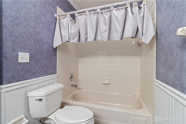 full bath featuring washtub / shower combination, wainscoting, and toilet