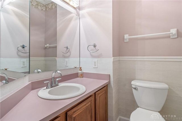 bathroom featuring a wainscoted wall, vanity, toilet, and tile walls