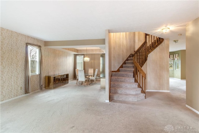 carpeted spare room featuring stairs, plenty of natural light, and wallpapered walls