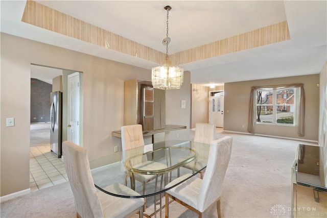 dining space featuring a chandelier, a raised ceiling, light carpet, and baseboards