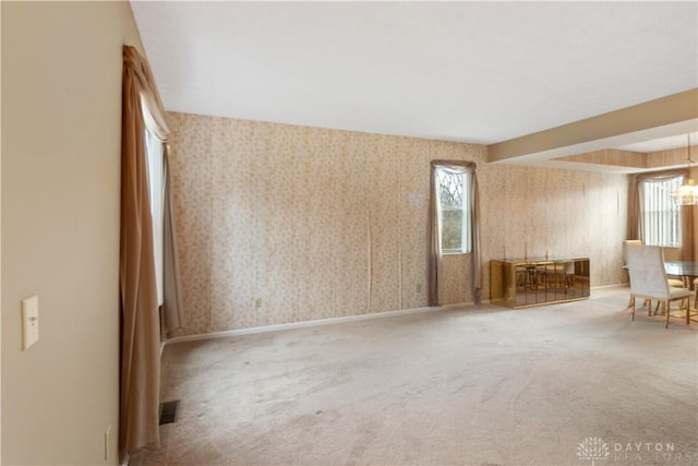 carpeted empty room with visible vents, a notable chandelier, baseboards, and wallpapered walls