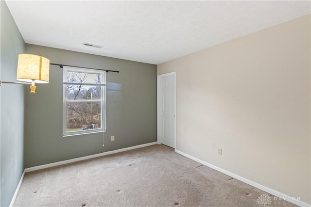 carpeted spare room with visible vents, a textured ceiling, and baseboards