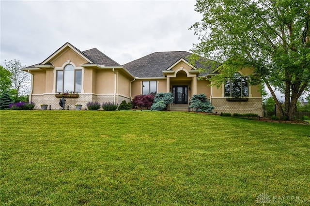 view of front facade featuring roof with shingles, brick siding, a front lawn, and stucco siding