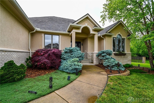 property entrance featuring stucco siding, a shingled roof, a yard, and brick siding