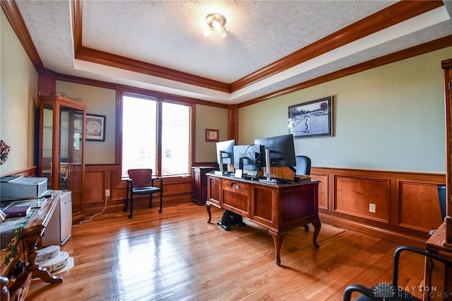 office space with light wood-type flooring, a tray ceiling, a wainscoted wall, and a textured ceiling