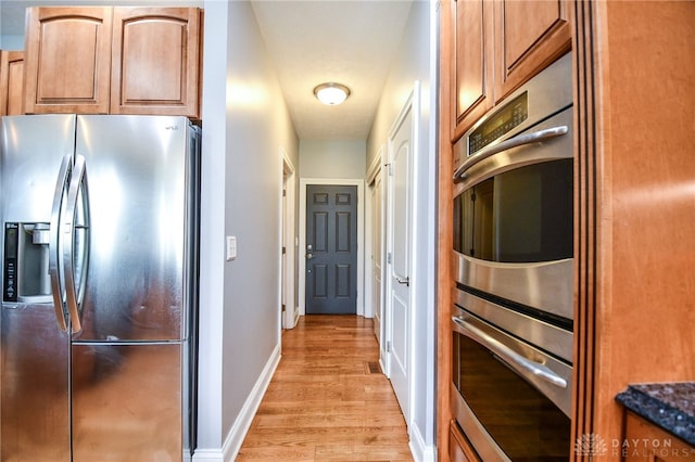 kitchen featuring brown cabinets, stainless steel appliances, light wood-style flooring, dark stone countertops, and baseboards