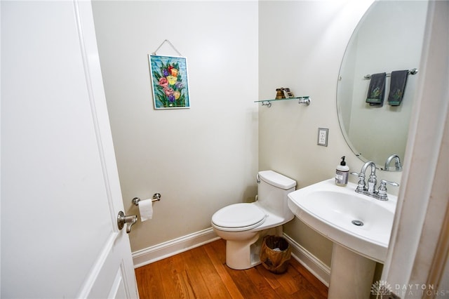 half bath featuring a sink, wood finished floors, toilet, and baseboards