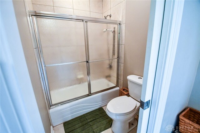 bathroom with toilet and bath / shower combo with glass door