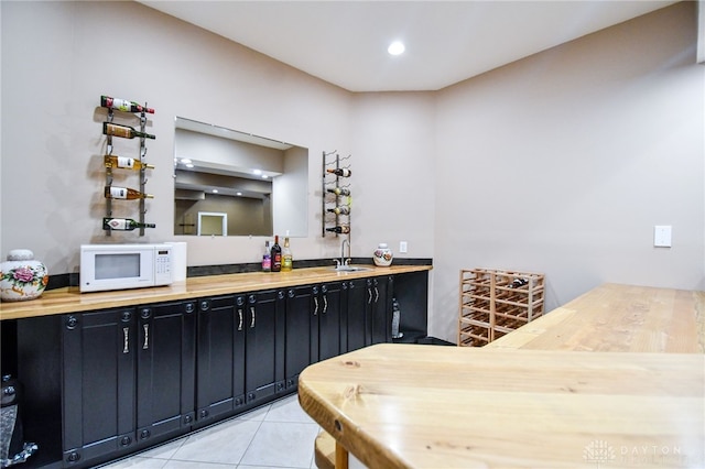 bar featuring light tile patterned floors, white microwave, and a sink