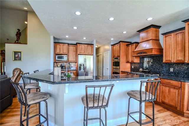 kitchen with light wood-style floors, custom exhaust hood, stainless steel appliances, and a kitchen breakfast bar