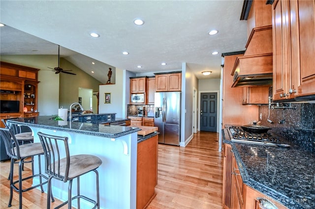 kitchen featuring stainless steel appliances, lofted ceiling, custom range hood, light wood-style floors, and a kitchen breakfast bar