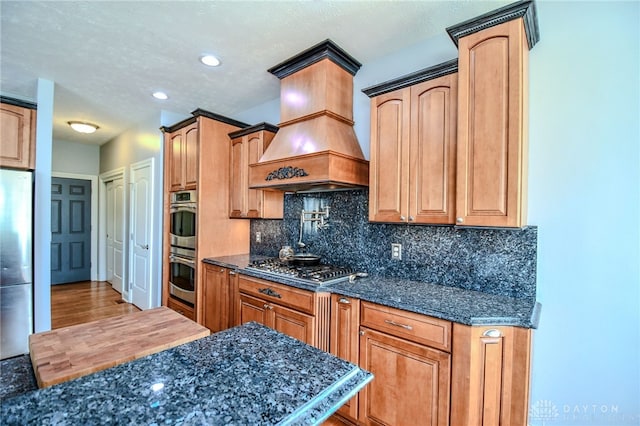 kitchen featuring appliances with stainless steel finishes, dark stone countertops, premium range hood, backsplash, and recessed lighting