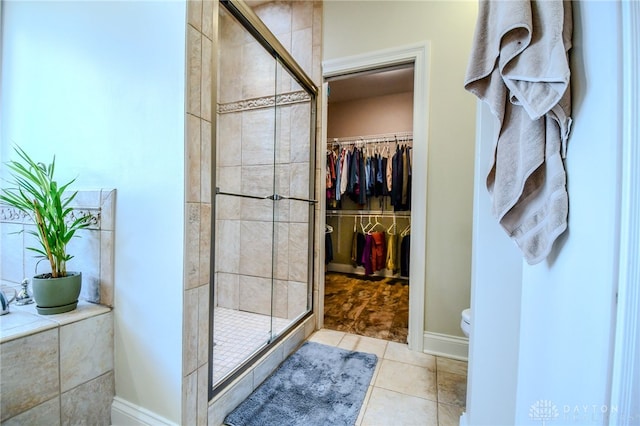 full bathroom with a stall shower, baseboards, toilet, tile patterned floors, and a spacious closet