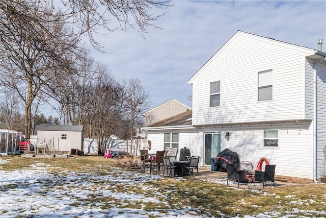 snow covered back of property with a storage shed, fence, a patio, and an outdoor structure