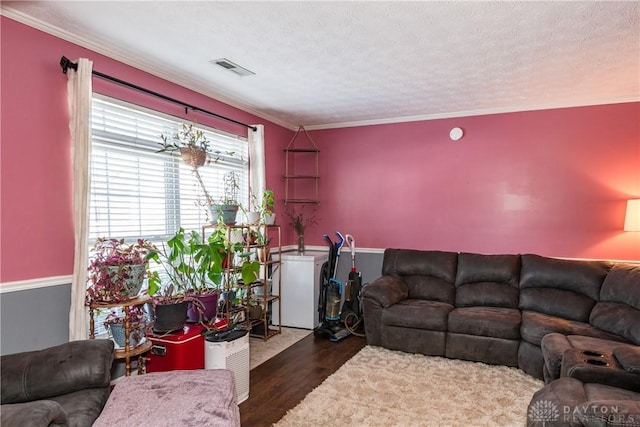 living area featuring a textured ceiling, ornamental molding, wood finished floors, and visible vents