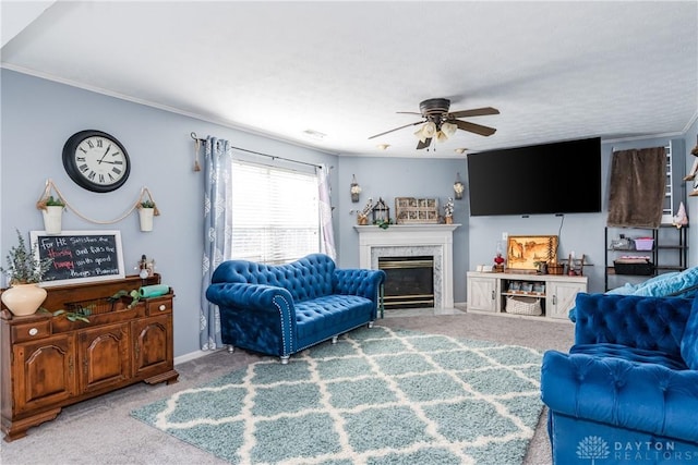 carpeted living room featuring ceiling fan, a fireplace, baseboards, and crown molding