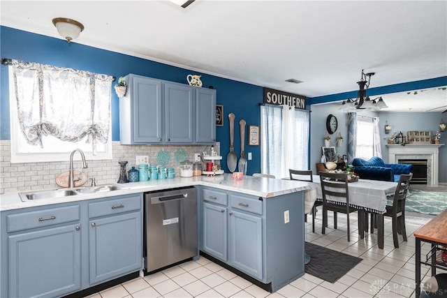 kitchen with dishwasher, a glass covered fireplace, a peninsula, light countertops, and a sink