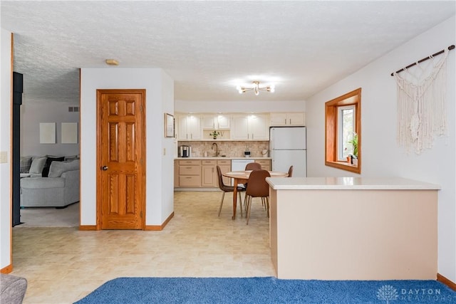 kitchen featuring white appliances, tasteful backsplash, a peninsula, light countertops, and a textured ceiling