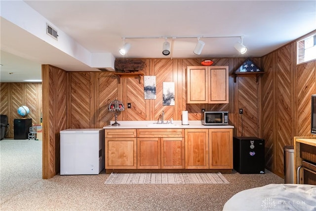 kitchen featuring wooden walls, visible vents, stainless steel microwave, refrigerator, and a sink