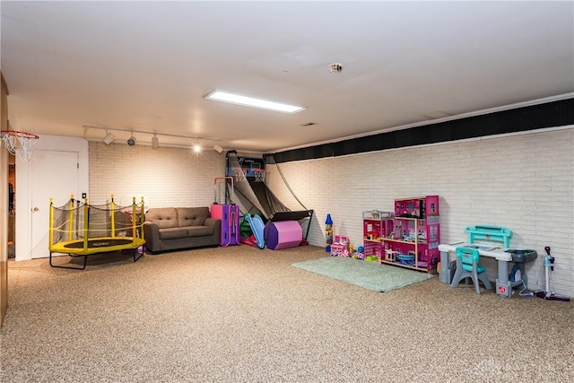 recreation room featuring brick wall, carpet, and track lighting