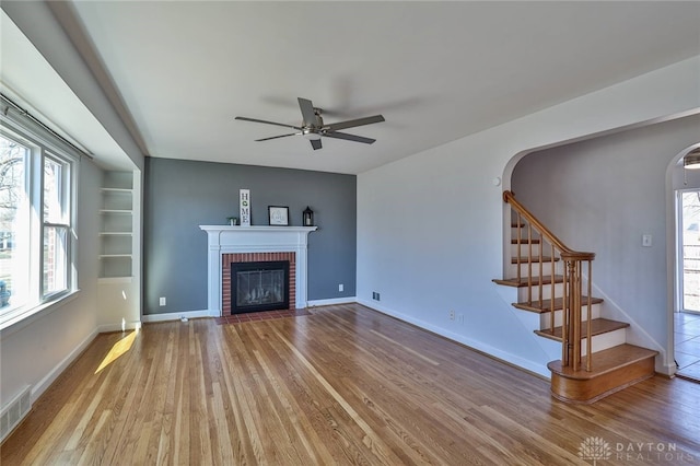 unfurnished living room with arched walkways, a brick fireplace, wood finished floors, and stairs