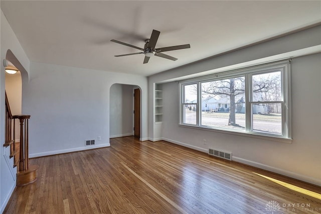 unfurnished living room featuring arched walkways, wood finished floors, visible vents, and baseboards