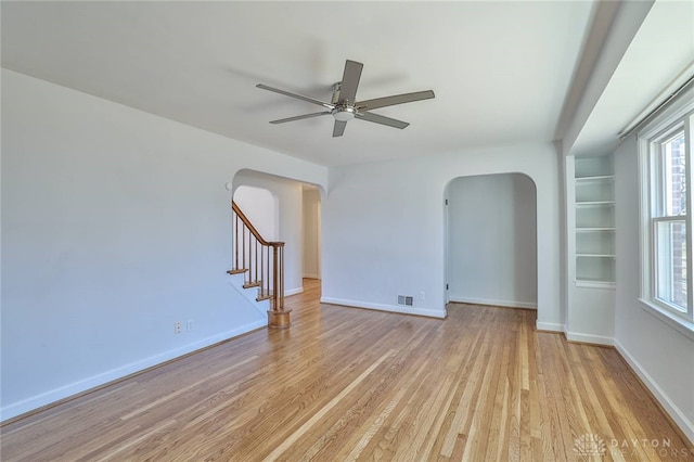 unfurnished room featuring stairway, light wood-style flooring, arched walkways, and baseboards