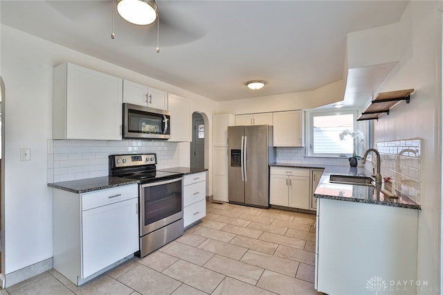 kitchen with arched walkways, white cabinets, stainless steel appliances, open shelves, and a sink