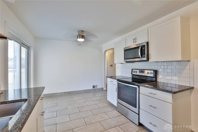 kitchen featuring arched walkways, stainless steel appliances, visible vents, tasteful backsplash, and dark stone countertops