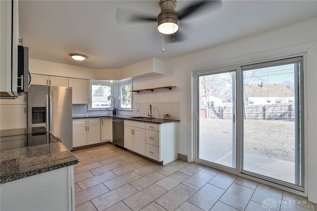 kitchen featuring tasteful backsplash, appliances with stainless steel finishes, white cabinets, a sink, and dark stone counters