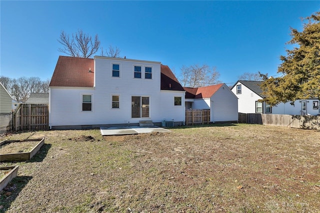 back of house featuring a yard, a patio area, a fenced backyard, and a garden