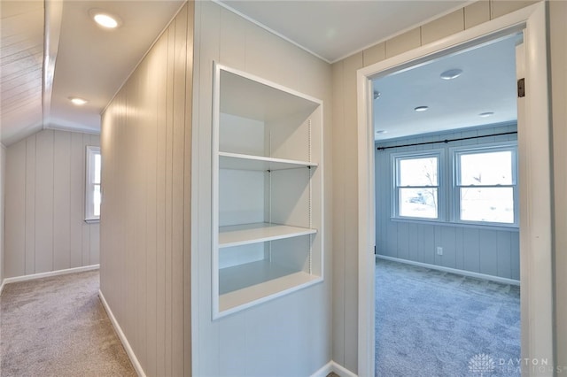 corridor with carpet floors, wooden walls, baseboards, and vaulted ceiling