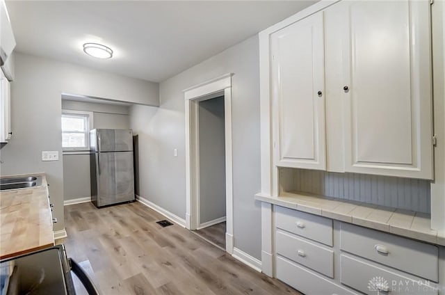 kitchen with white cabinetry, baseboards, light wood-style floors, light countertops, and freestanding refrigerator