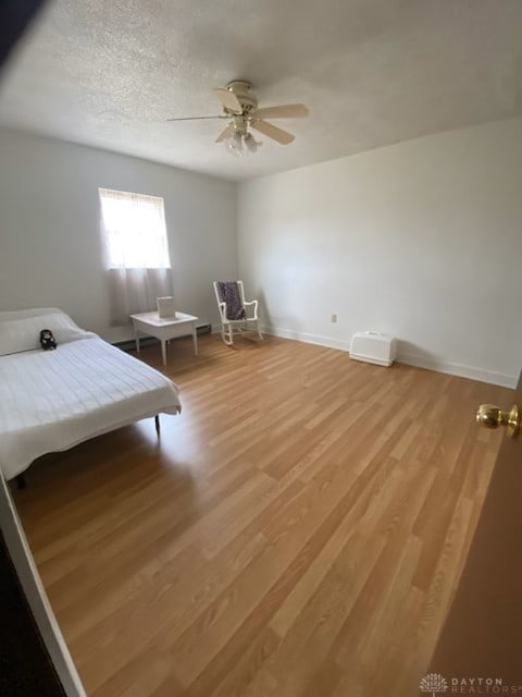 bedroom featuring light wood-type flooring, ceiling fan, baseboards, and a textured ceiling