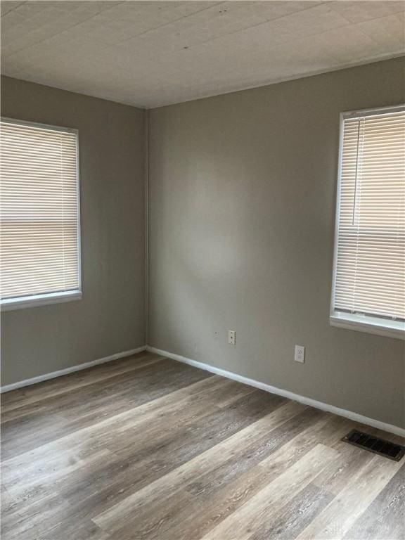 unfurnished room featuring wood finished floors, visible vents, and baseboards