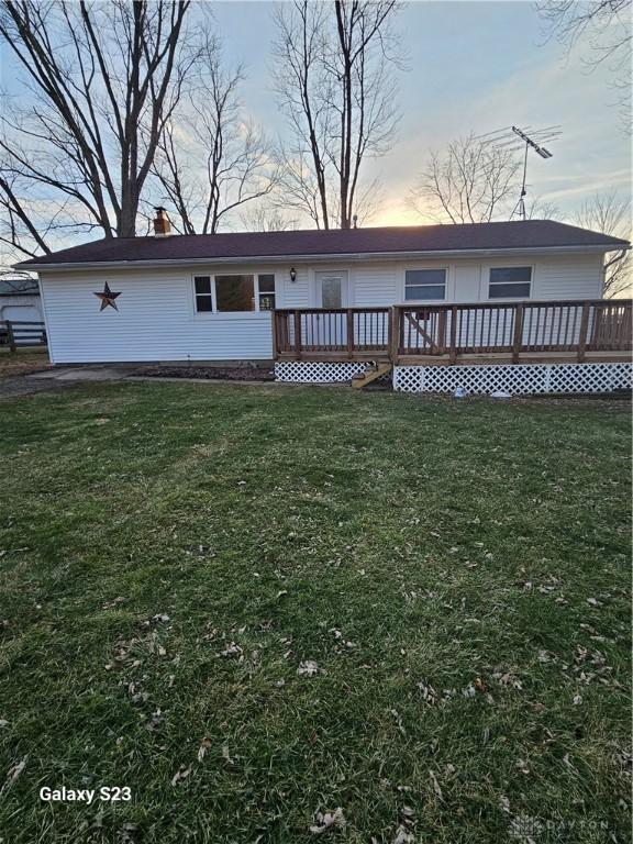 back of property at dusk with a yard, a chimney, and a wooden deck