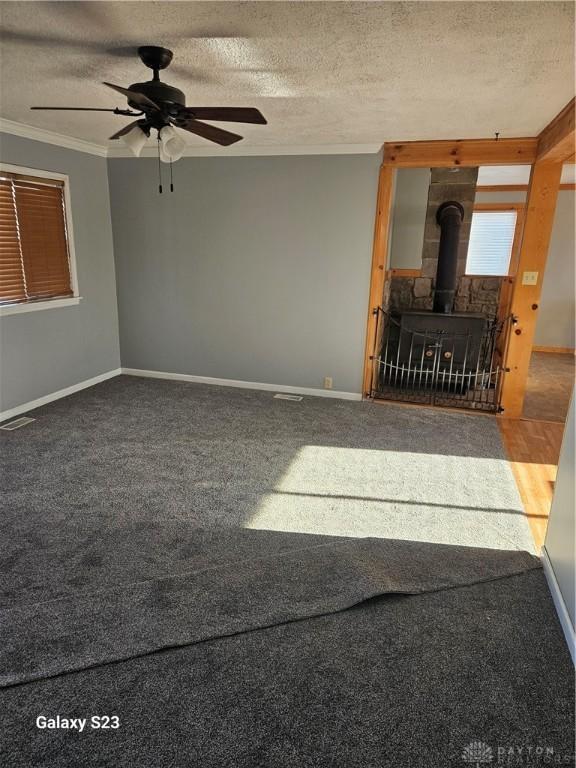 carpeted spare room featuring a wood stove, a textured ceiling, visible vents, and crown molding