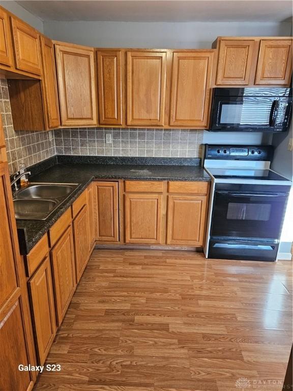 kitchen with tasteful backsplash, a sink, light wood finished floors, and black appliances